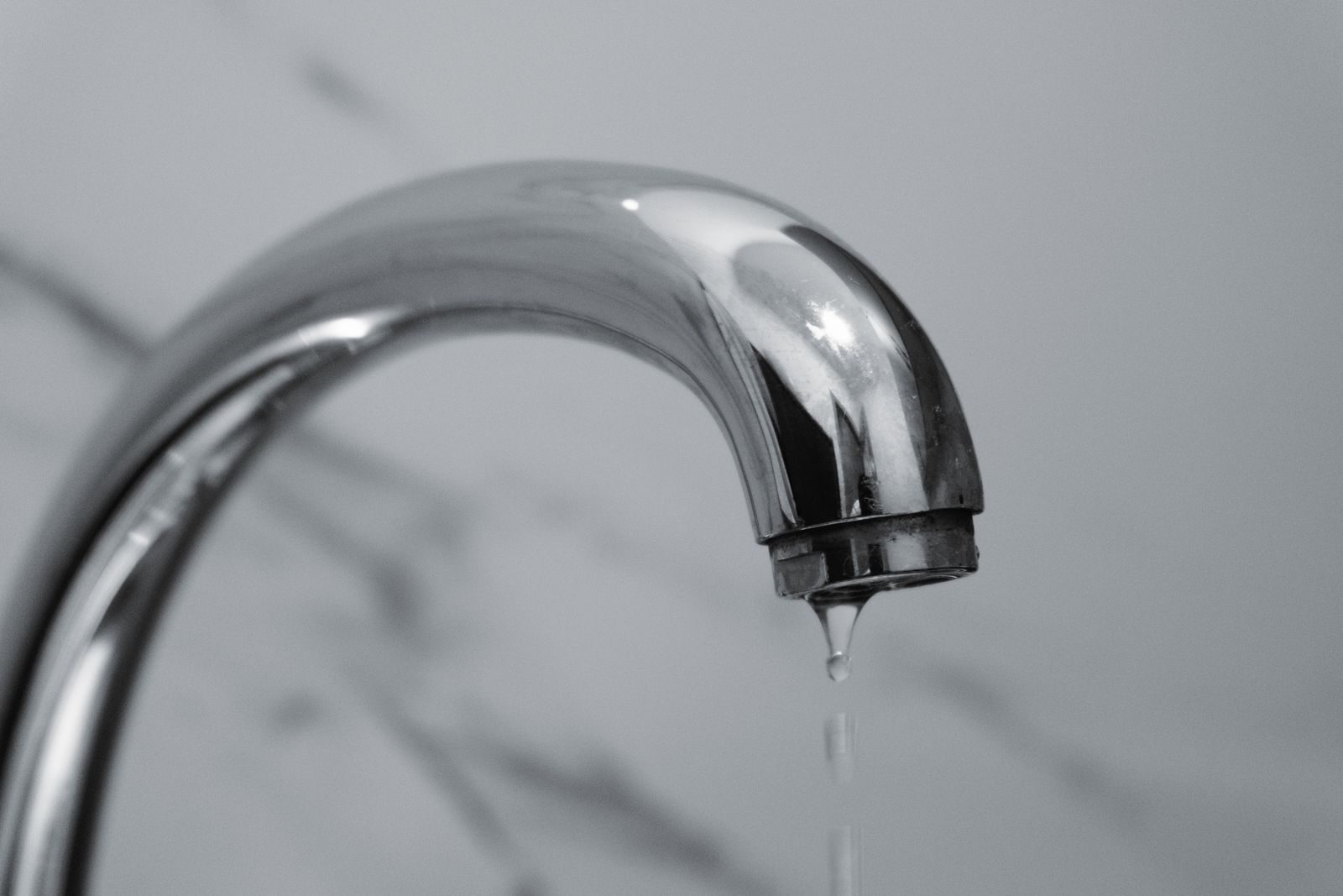 Close-up of a chrome bathroom faucet dripping water on a tiled wall